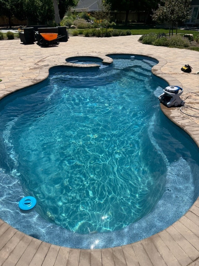 A beautifully designed inground pool in Spanish Springs, featuring a freeform shape, integrated spa, and spacious stone patio surrounded by lush landscaping.