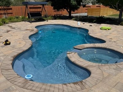 A beautifully designed inground pool in Spanish Springs, featuring a freeform shape, integrated spa, and spacious stone patio surrounded by lush landscaping.
