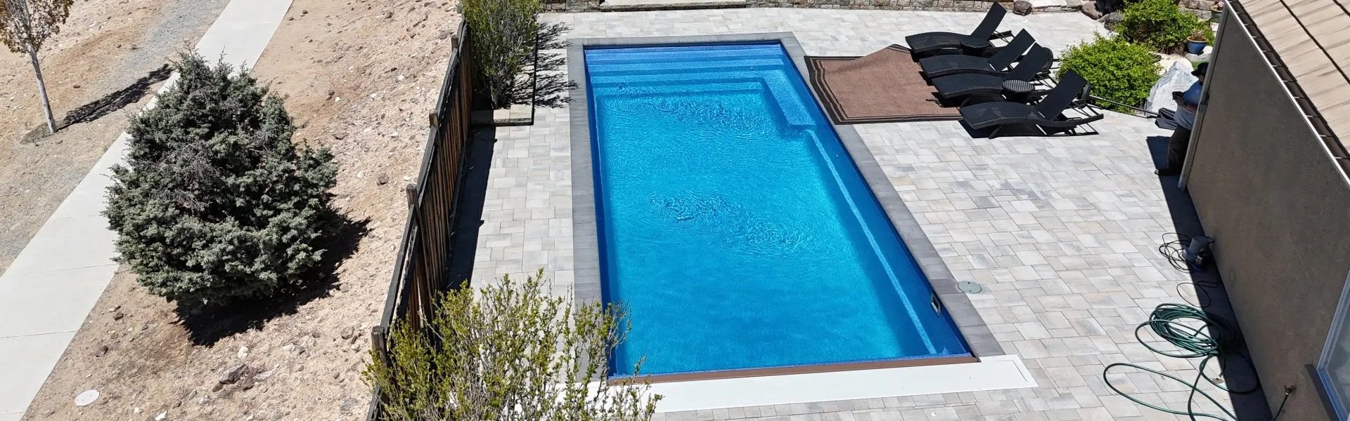 A fiberglass pool in a backyard next to an enclosed fence and some lawn chairs.