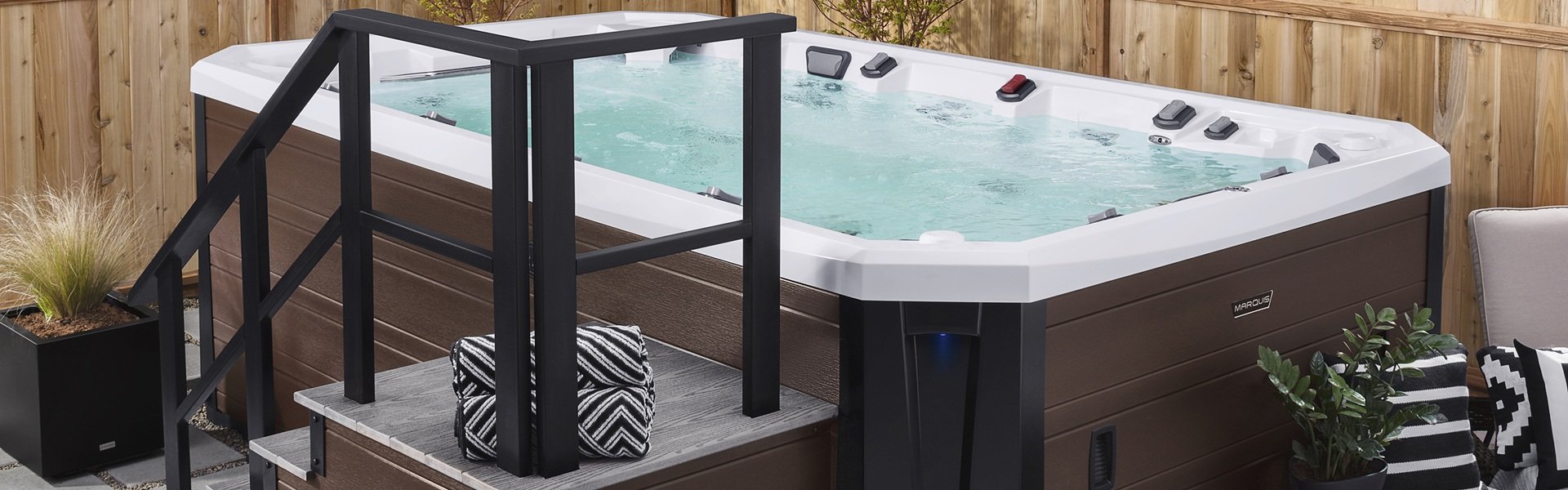 A swim spa in someone's backyard. There is stairs that lead up into the spa. It is surrounded by a fence.