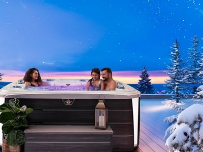 A family of 3 sit in a hot tub at night during winter. They are surrounded by a snowy ambiance.