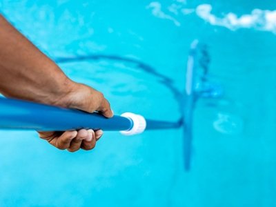 A man's hand cleaning his swimming pool with a skimmer net.