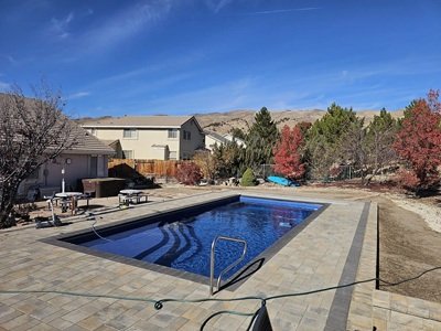 An inground swimming pool in a residential backyard. There is a fence surrounding the pool. A line goes across the the front of the pool and into the pool to clean it.