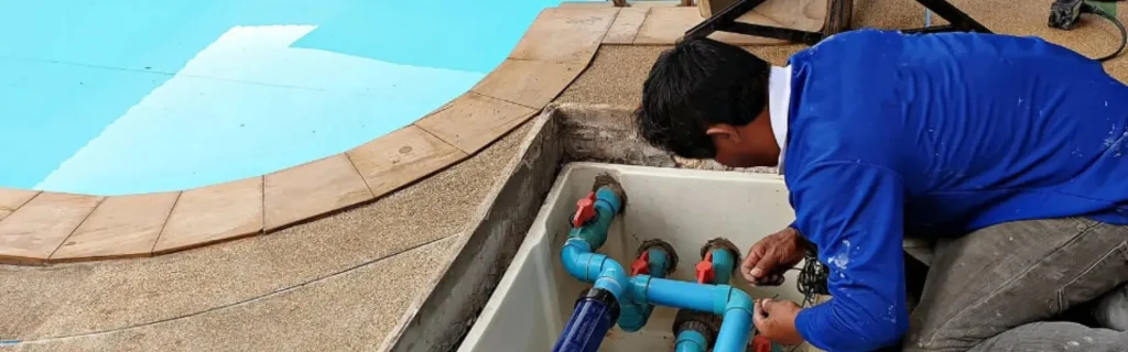 Pool technician repairing pool equipment and plumbing next to a swimming pool
